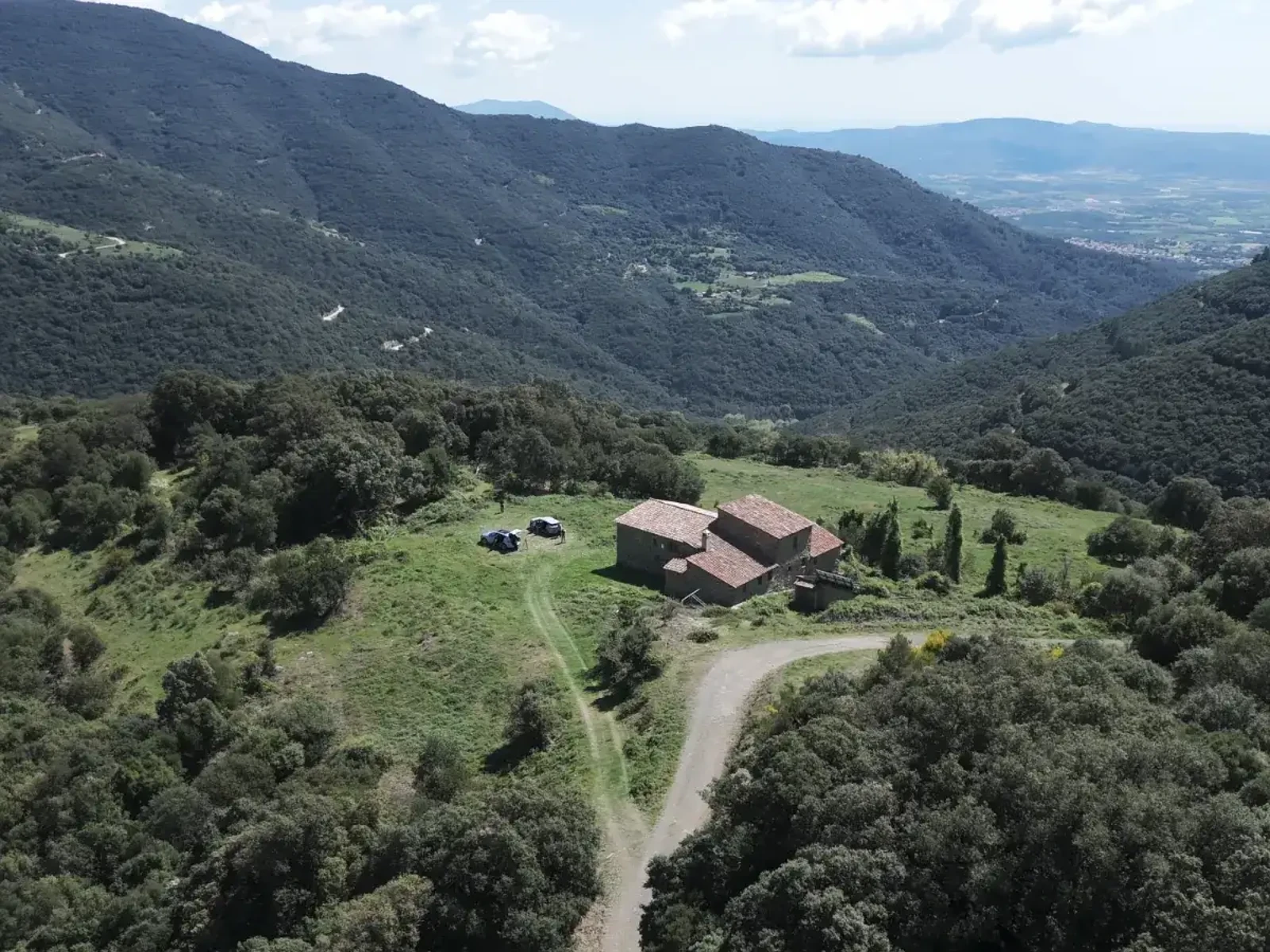 Masía de piedra en un claro entre montañas boscosas.